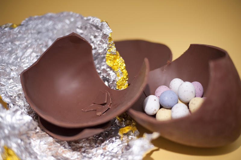 Broken pieces of a large chocolate Easter Egg with small sugar candy eggs inside.