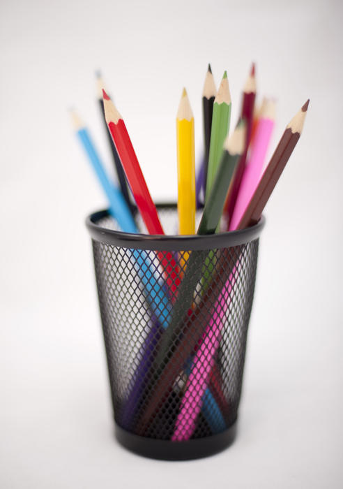 Coloured pencils standing upright in a desk tidy with their sharpened colourful points at the top