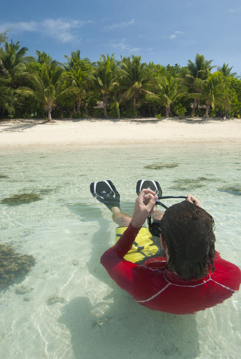Snorkeler lying on his back floating offshore in crystal clear shallow water donning his mask