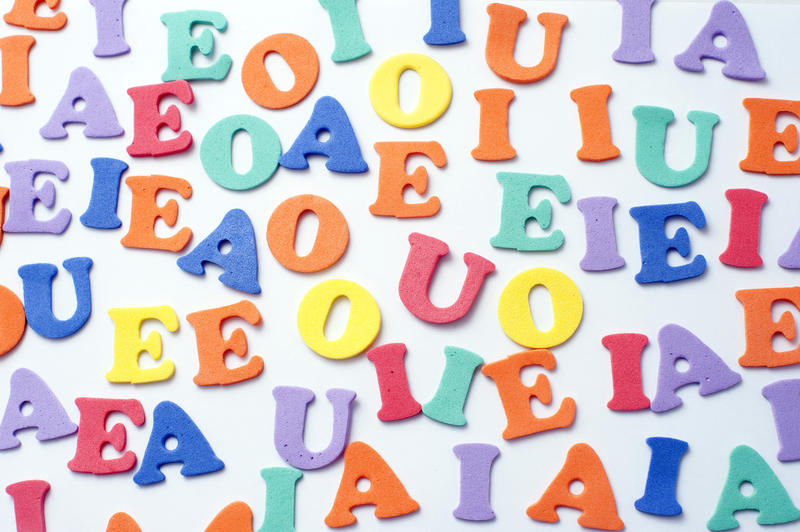 Random collection of educational alphabet letters, confined to the vowels, scattered on a white background