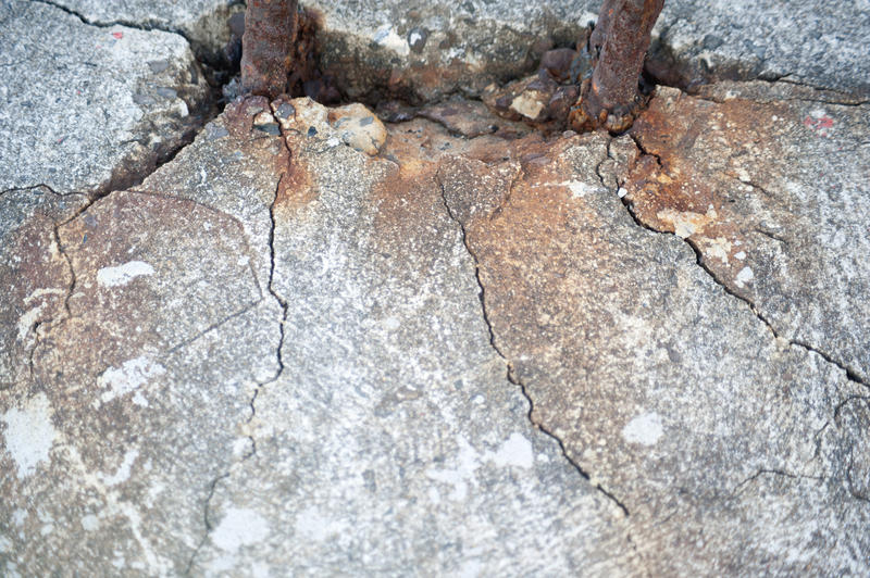 Close Up of Two Rusted Rebar Mounted in Cracked Cement of Structure with Rust Stains