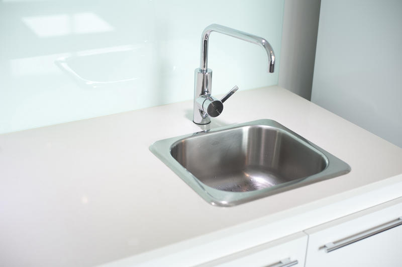 Stainless steel sink and faucet in a white kitchen cabinet with a clean empty counter alongside
