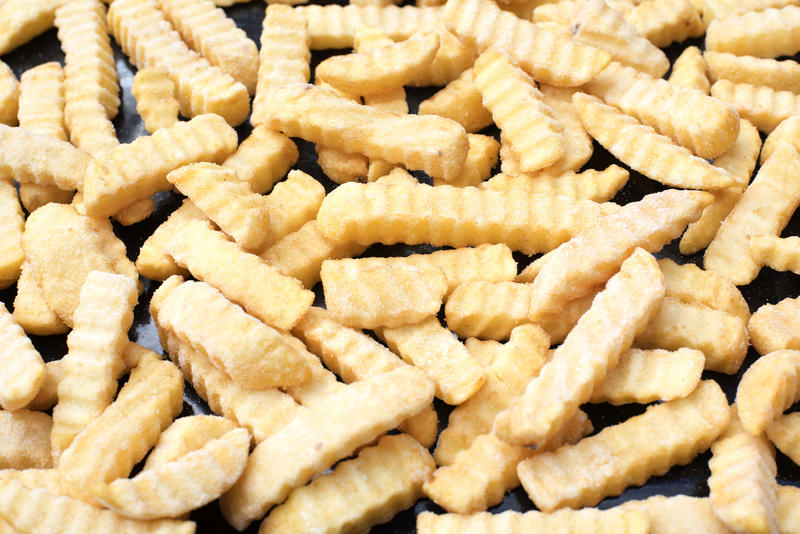 Frozen crinkle cut potato chips laid out on a meta tray ready for baking in the oven