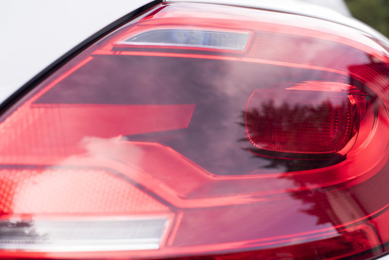 Red plastic lens of a rear light on a car or automobile with a view of the globe inside and reflections of trees