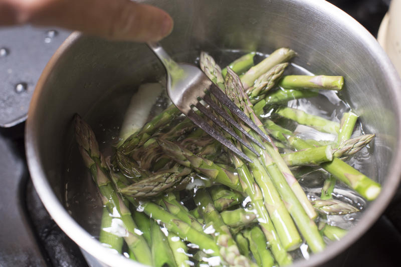 High Angle Close Up of Person Cooking Cut Asparagus Spears with Fork in Pot on Stove Top - Unrecognizable Person Boiling Asparagus