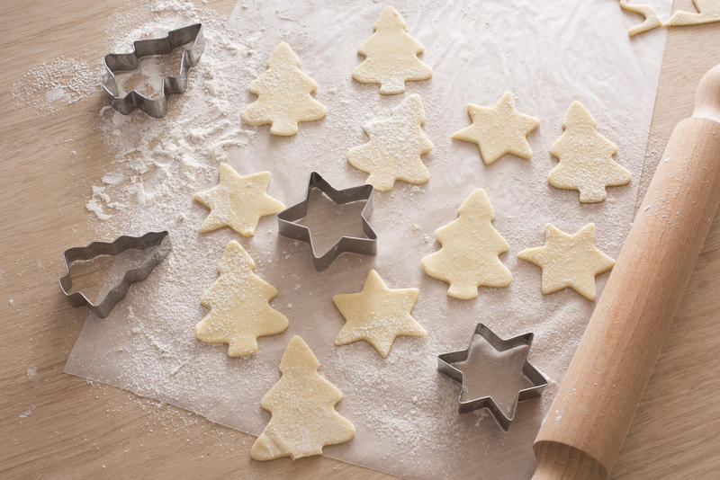 Cooking festive homemade Christmas biscuits with cut out pastry shapes alongside a star and tree shaped cookie cutter and wooden rolling pin on a kitchen counter