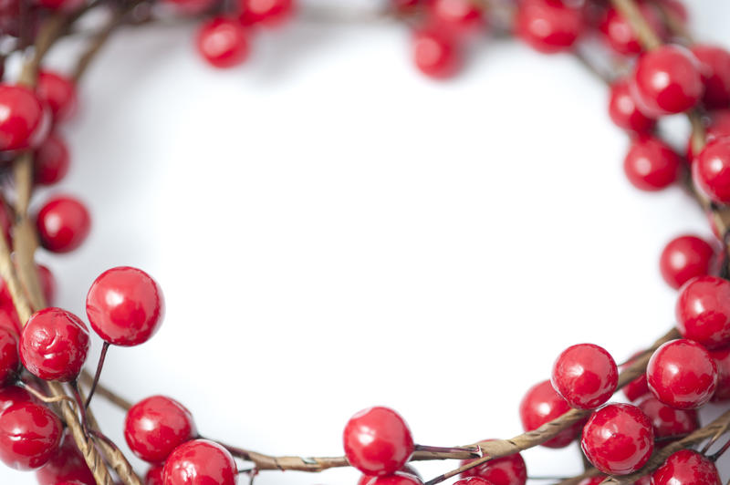 Border, wreath or frame of artificial festive red Christmas berries around central white copy space for your holiday message