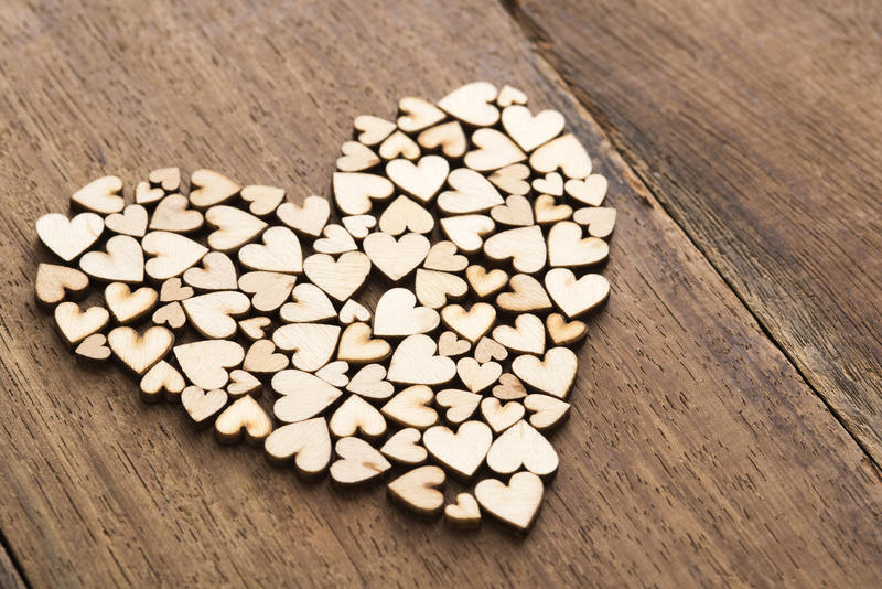 Close-up pile of craft wooden hearts cut of unpainted plywood formed in shape of bigger heart over lacquered table surface, love concept