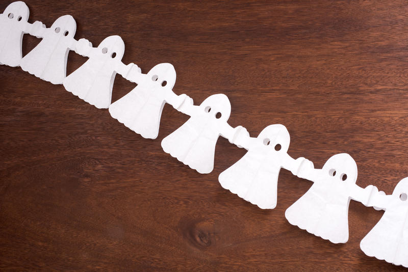 halloween ghost paper chain decorations on a wooden surface, pictured at an angle with space for text above and below